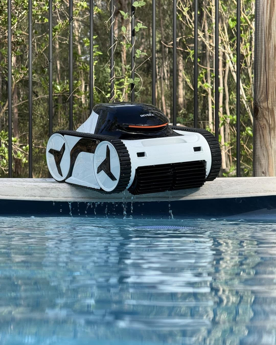 A robotic pool cleaner resting on the coping of a serviced pool, water running off its tracks.