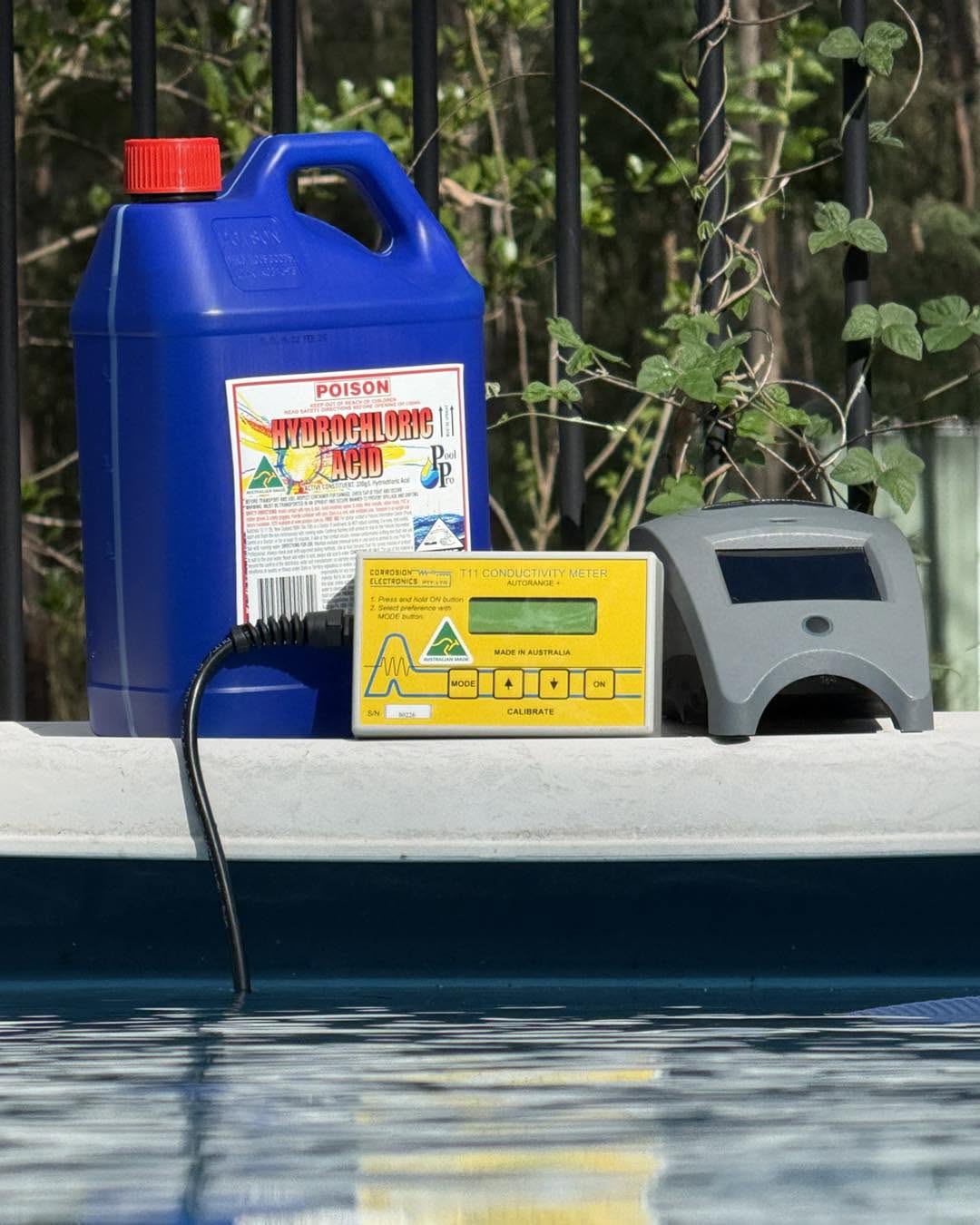 A conductivity meter and a drum of pool acid on the edge of a pool, with the water below.